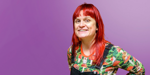 Woman with red hair and green and red t-shirt and overalls smiling to the camera