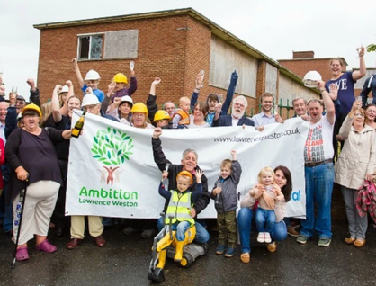 Large group of people, some wearing hard hats, cheering in front of a banner reading 