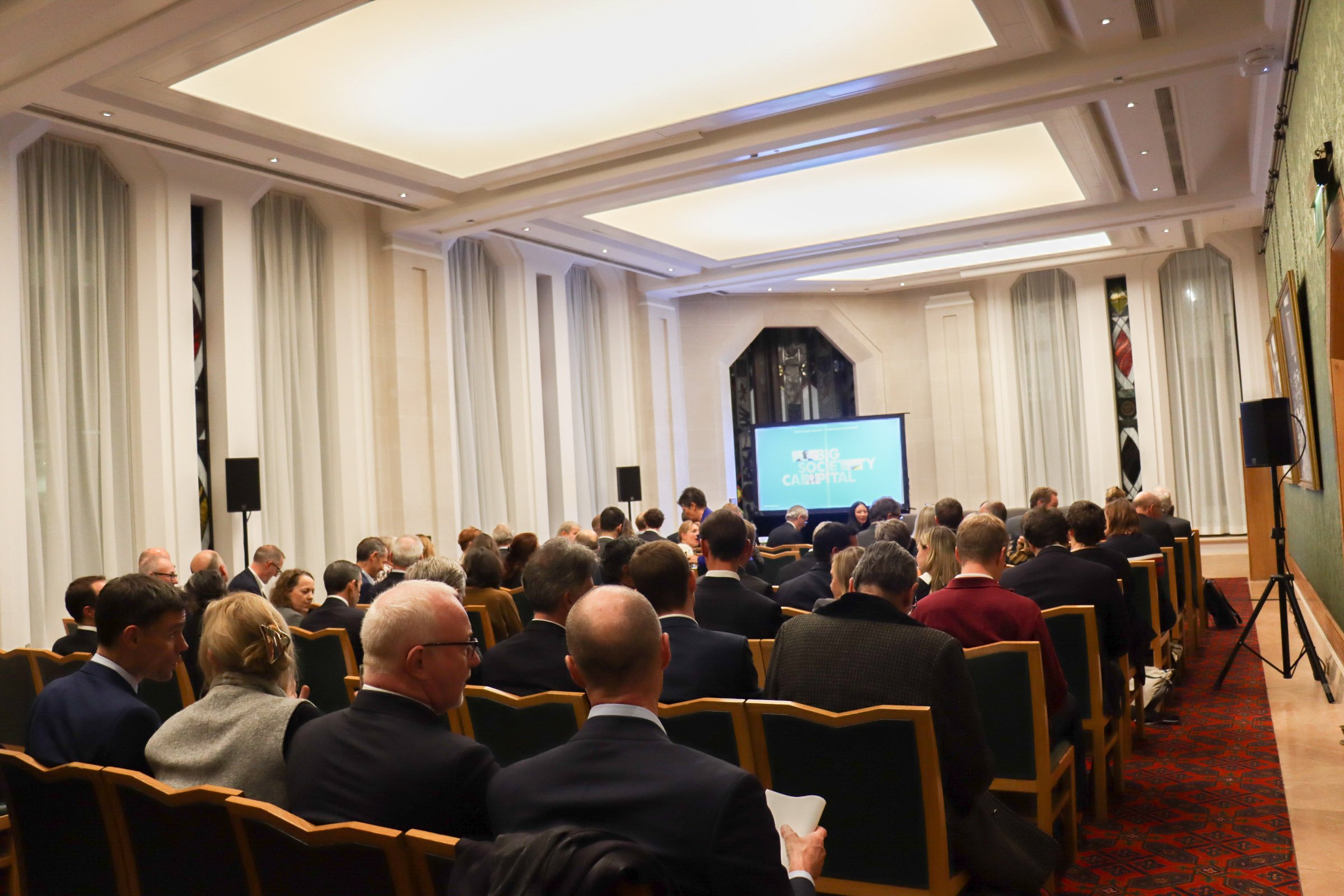 Event hall with many people sat looking at a screen