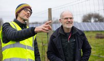Two men, one in a high visibility jacket, pointing and talking with solar panels in the background