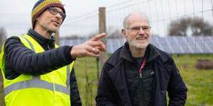 Two men, one in a high visibility jacket, pointing and talking with solar panels in the background