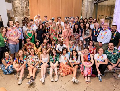 Image of a large number of people posing, wearing colourful clothing and some with flower lanyards around their necks