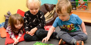 Three young children sitting and reading a book