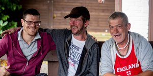 Three men sitting on a bench smiling and laughing