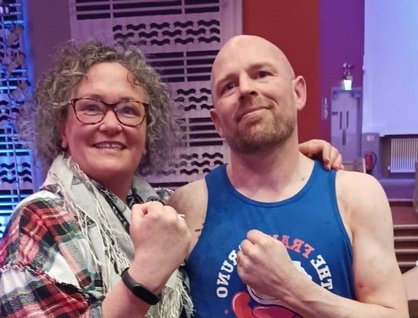 Man and woman in a boxing gym, smiling at the camera and holding up their fists