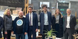 Six people, including Ed Miliband MP, at a scrap works smiling to the camera
