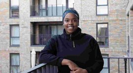 A tenant at the Campbell Wharf development standing on a balcony smiling at the camera
