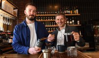 Two men pouring tea leaves behind a bar