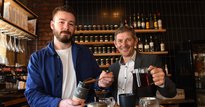 Two men pouring tea leaves behind a bar