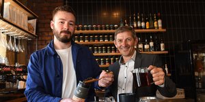 Two men pouring tea leaves behind a bar