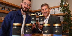 Two men holding up tins of tea