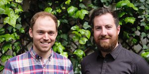 Two men smiling infront of a green bush