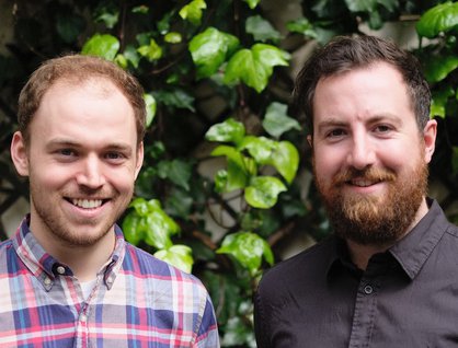 Two men smiling infront of a green bush