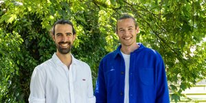 Two men in smart casual clothing standing in front of a tree, smiling