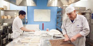 Two men in a bakery kitchen where one is slicing brownies
