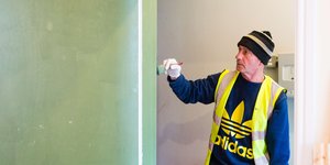 Main wearing a high visibility jacket and a beanie painting a wall