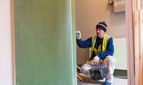 Main wearing a high visibility jacket and a beanie painting a wall