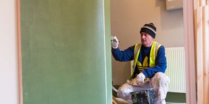 Main wearing a high visibility jacket and a beanie painting a wall