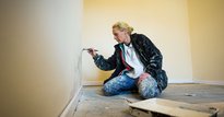 Woman sat on floor painting a wall