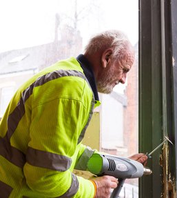 Man wearing a high visibility jacket strimming the paint off a window