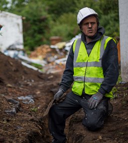 Man wearing a high visibility jacket and a hard hat sitting in a construction sit