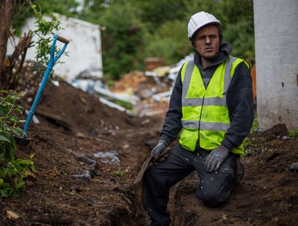 Man wearing a high visibility jacket and a hard hat sitting in a construction sit