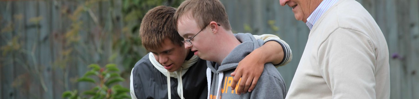 One elderly man standing in a garden with two young men with learning disabilities