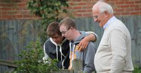 One elderly man standing in a garden with two young men with learning disabilities