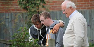 One elderly man standing in a garden with two young men with learning disabilities