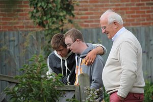 One elderly man standing in a garden with two young men with learning disabilities