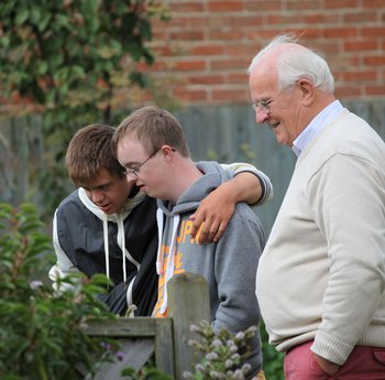 One elderly man standing in a garden with two young men with learning disabilities