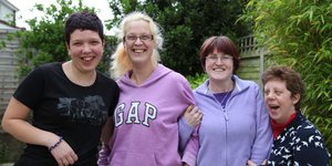 Four women smiling and linking arms