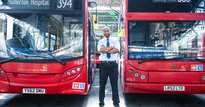 Man standing proudly in front of two red buses