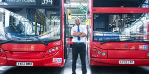Man standing proudly in front of two red buses