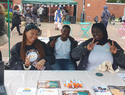 Three people sitting at a desk with pens and leaflets, posing for the camera