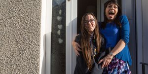 Mum holding daughter in school uniform and both are smiling