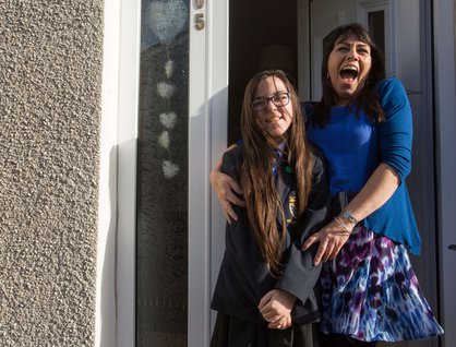 Mum holding daughter in school uniform and both are smiling