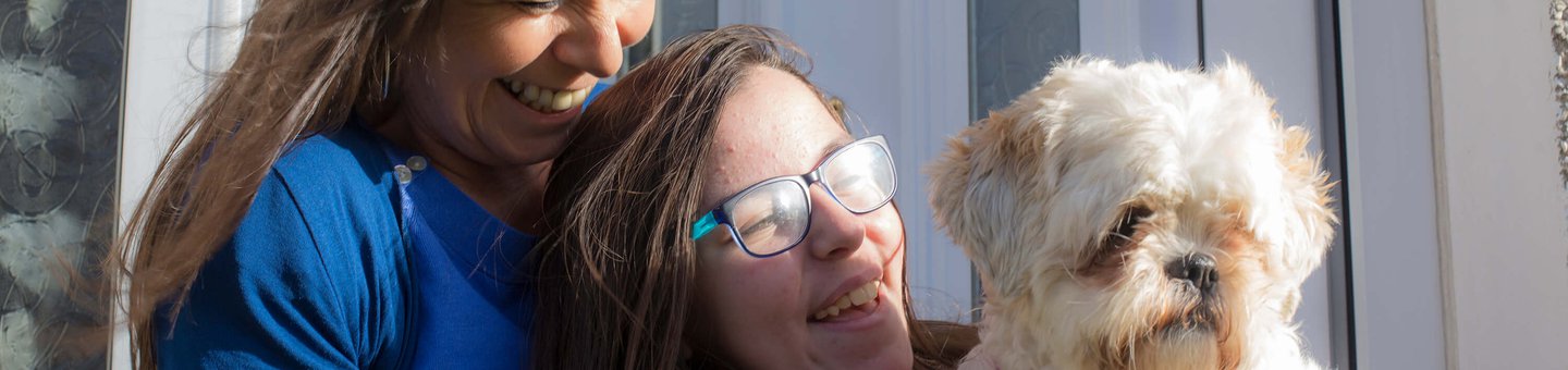 Two women sitting on a porch smiling with a small white dog