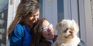 Two women sitting on a porch smiling with a small white dog