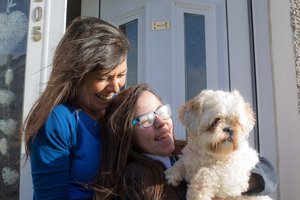 Two women sitting on a porch smiling with a small white dog