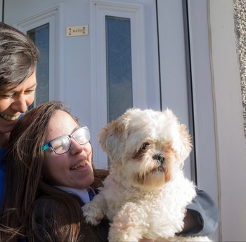 Two women sitting on a porch smiling with a small white dog