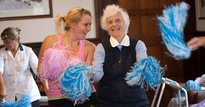 An elderly woman exercising with pom poms with a dance instructor