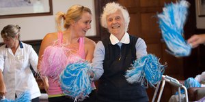 An elderly woman exercising with pom poms with a dance instructor