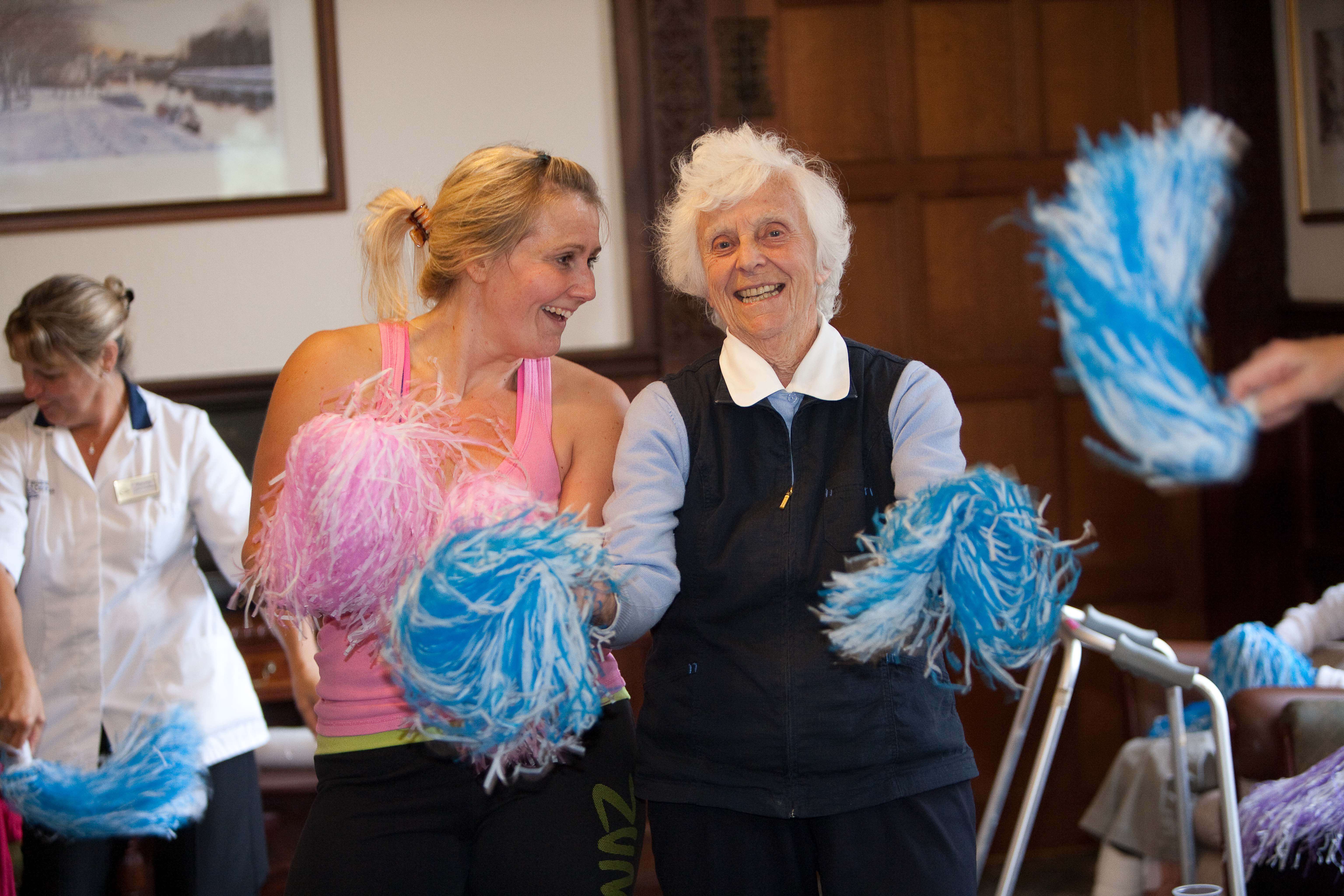 An elderly woman exercising with pom poms with a dance instructor