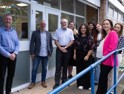 Group of ten people in smart-casual clothing posing for the camera in front of a door