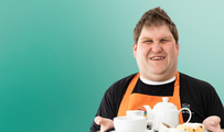 Waiter wearing an orange apron holding a tray of food and hot drinks