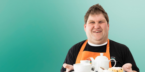 Waiter wearing an orange apron holding a tray of food and hot drinks