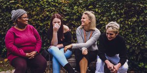 Three women sitting on a bench laughing