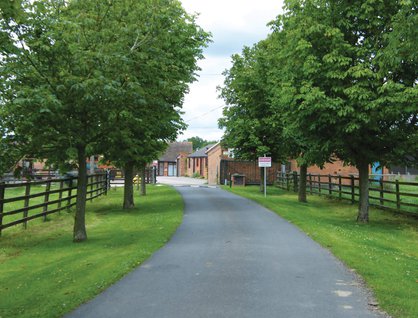 A winding road bordered by trees leading to a group of red brick buildings