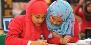 Two young girls wearing hijabs doing school work